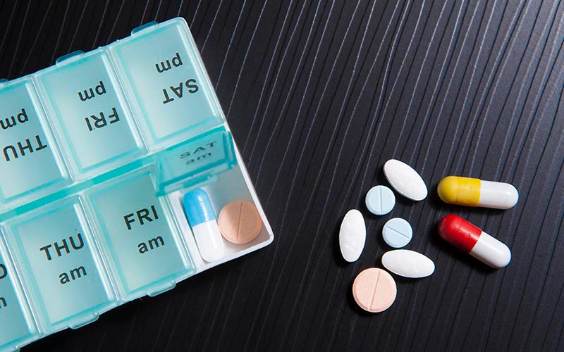 A weekly pill organiser alongside prescription medication